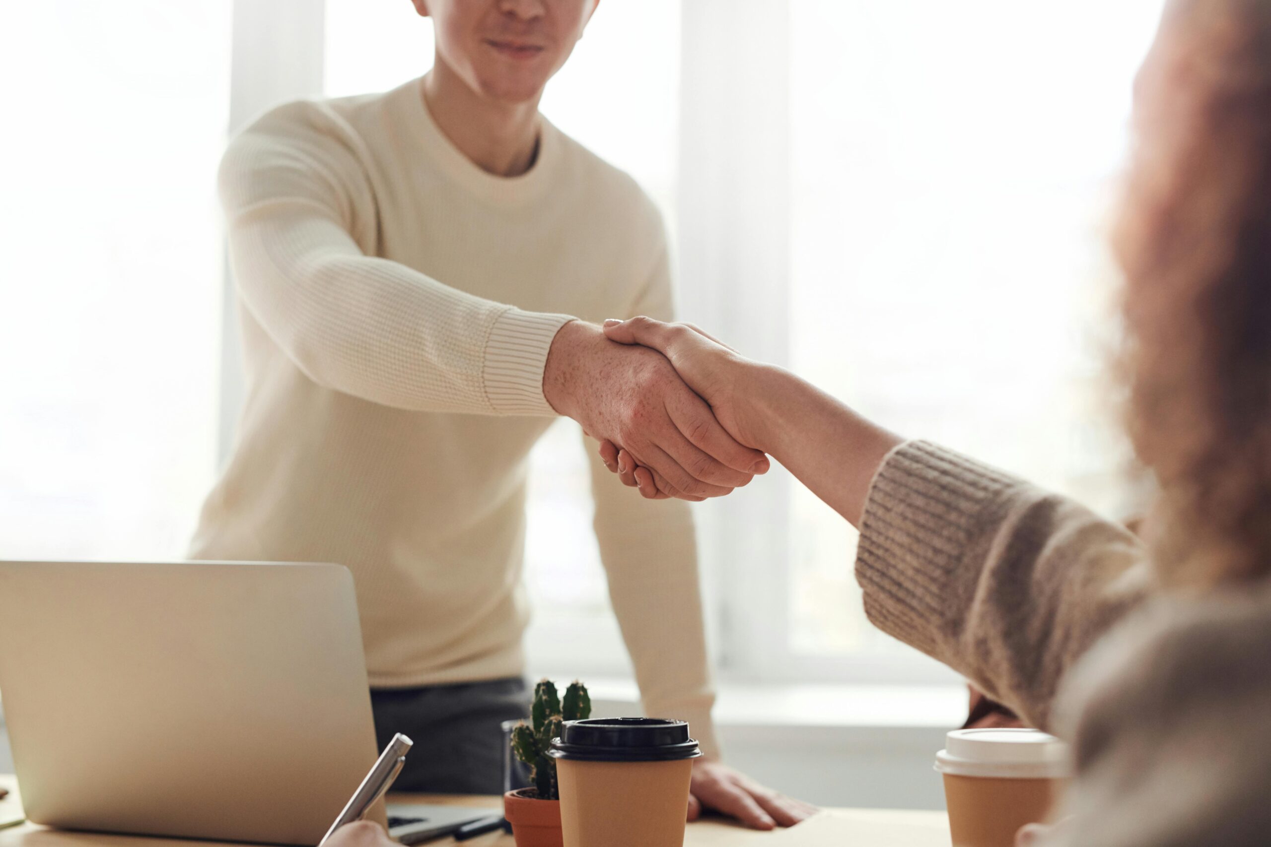 A person standing up to shake a second person's hand across a desk
