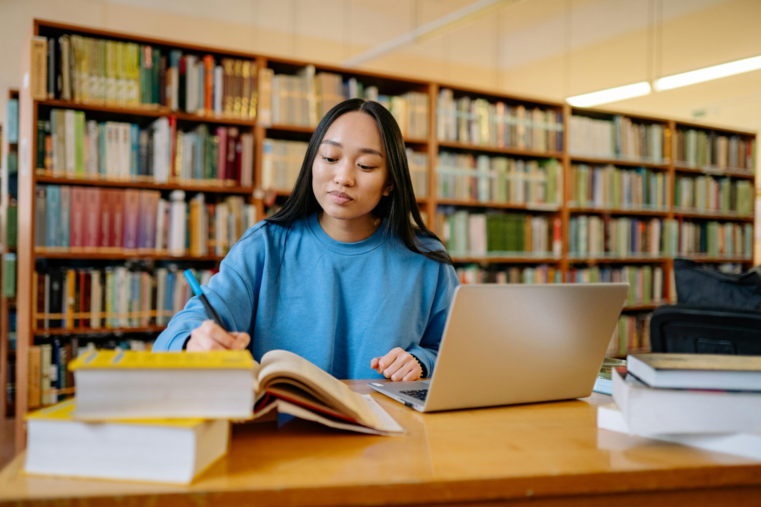 A young woman sitting at a desk in a library with an open latop and books in front of her