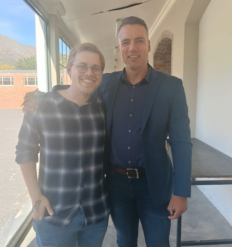 Two men standing together, smiling at the camera.