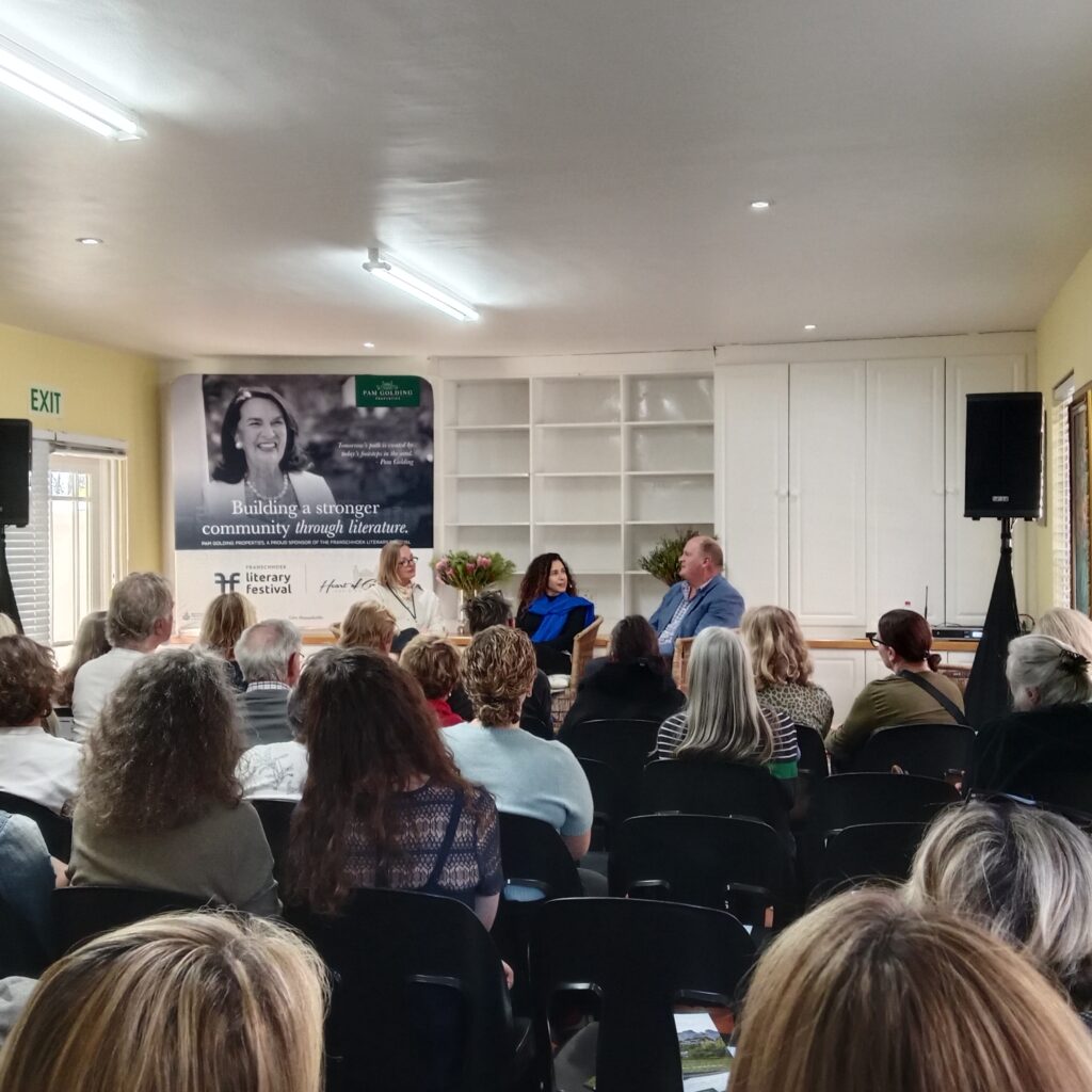 Three people sitting in chairs at the front of the room, facing an audience.