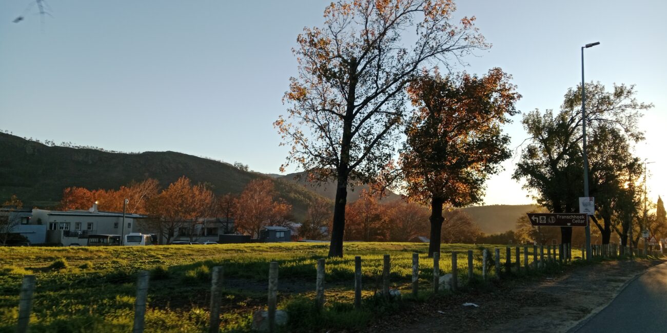 A landscape showing hills, a field, autumn trees, and posts.