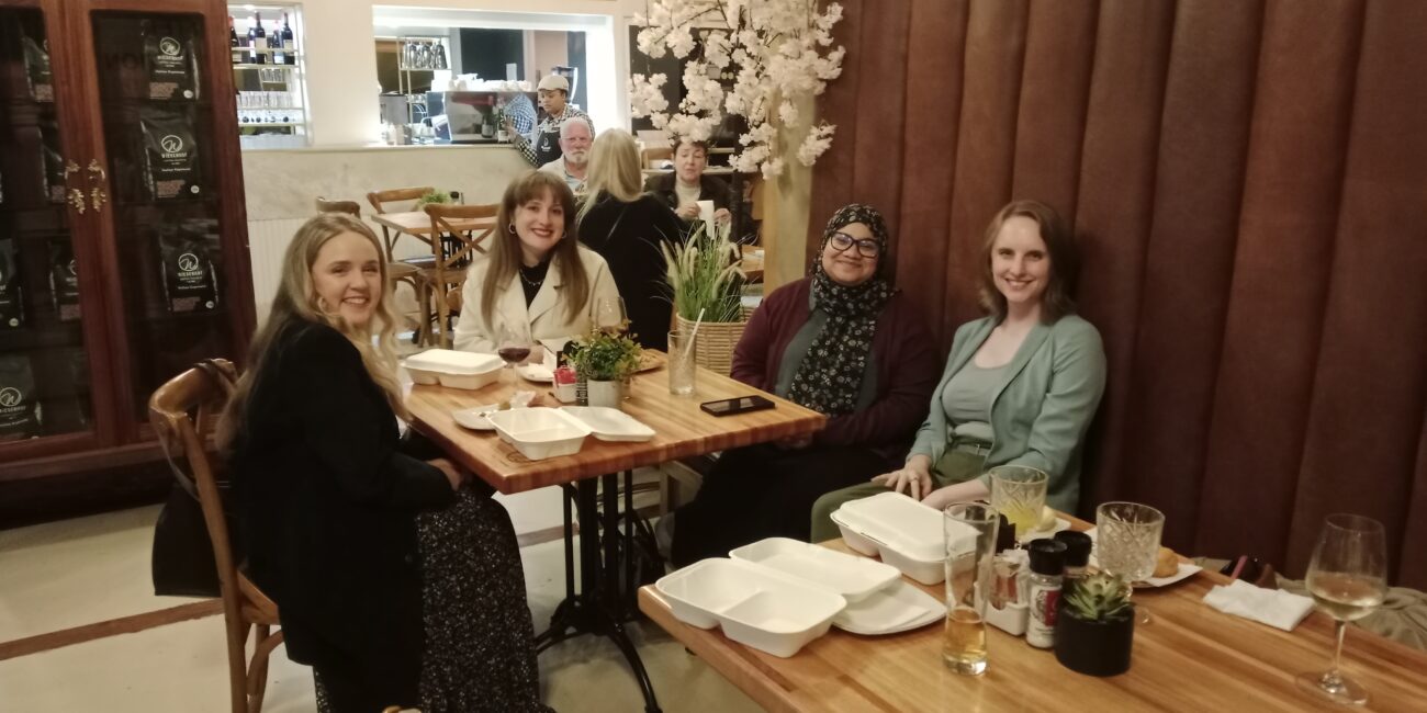 Four women sitting around a table in a restaurant and smiling at the camera.